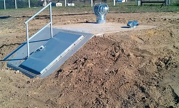 Below-ground storm shelter with steel door and vent, backfilled and ready